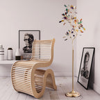 Clérachic agate floor lamp next to a sculptural slatted wooden chair, with framed portraits on a pale floor.