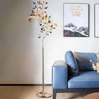 Clérachic agate floor lamp lit against a pale wall, beside a blue leather sofa and a framed mountain print.