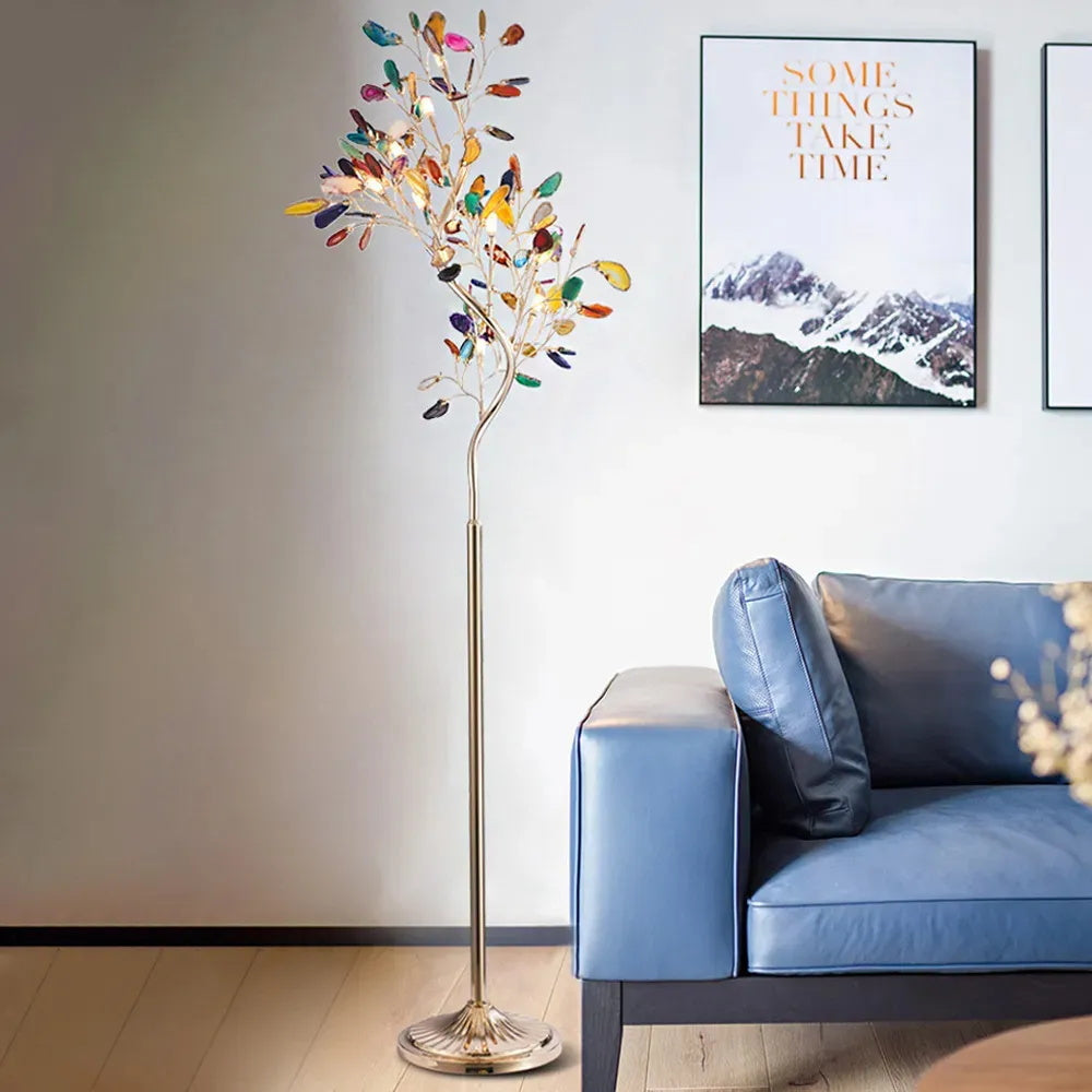 Clérachic agate floor lamp lit against a pale wall, beside a blue leather sofa and a framed mountain print.
