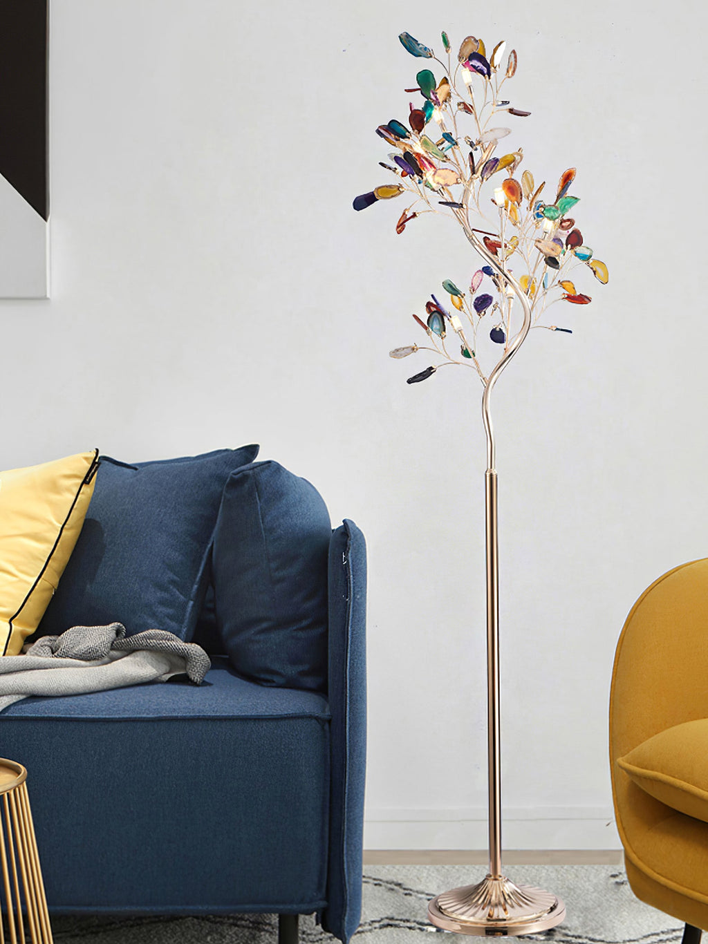 Clérachic agate floor lamp lit in front of a blue sofa with a yellow cushion, against a pale wall.