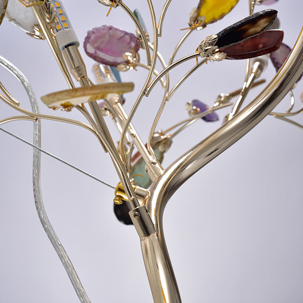 Close view of a Clérachic floor lamp stem splitting into branches, with a bulb, a glass cable and agate slices on gold clips.
