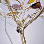 Close view of a Clérachic floor lamp stem splitting into branches, with a bulb, a glass cable and agate slices on gold clips.