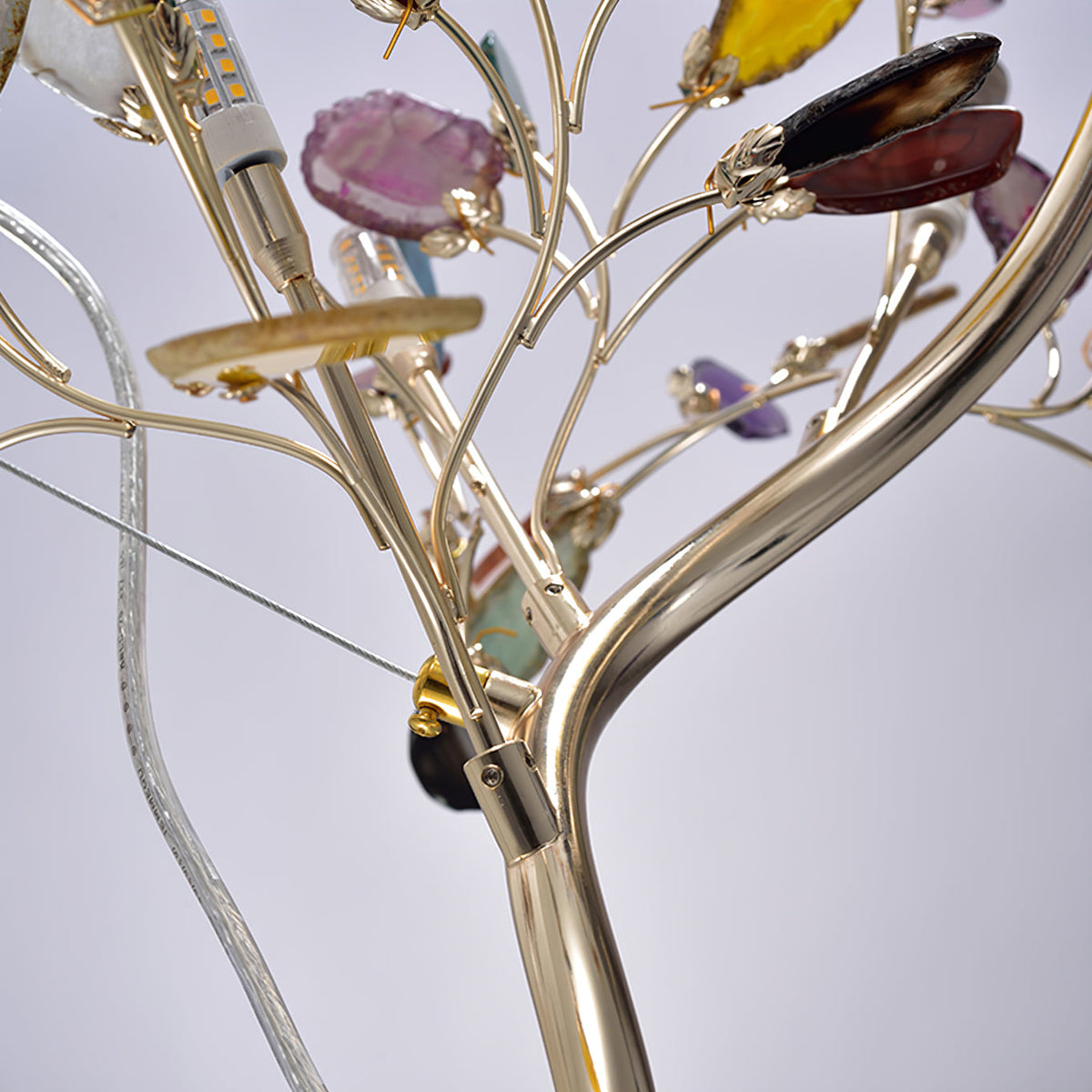 Close view of a Clérachic floor lamp stem splitting into branches, with a bulb, a glass cable and agate slices on gold clips.