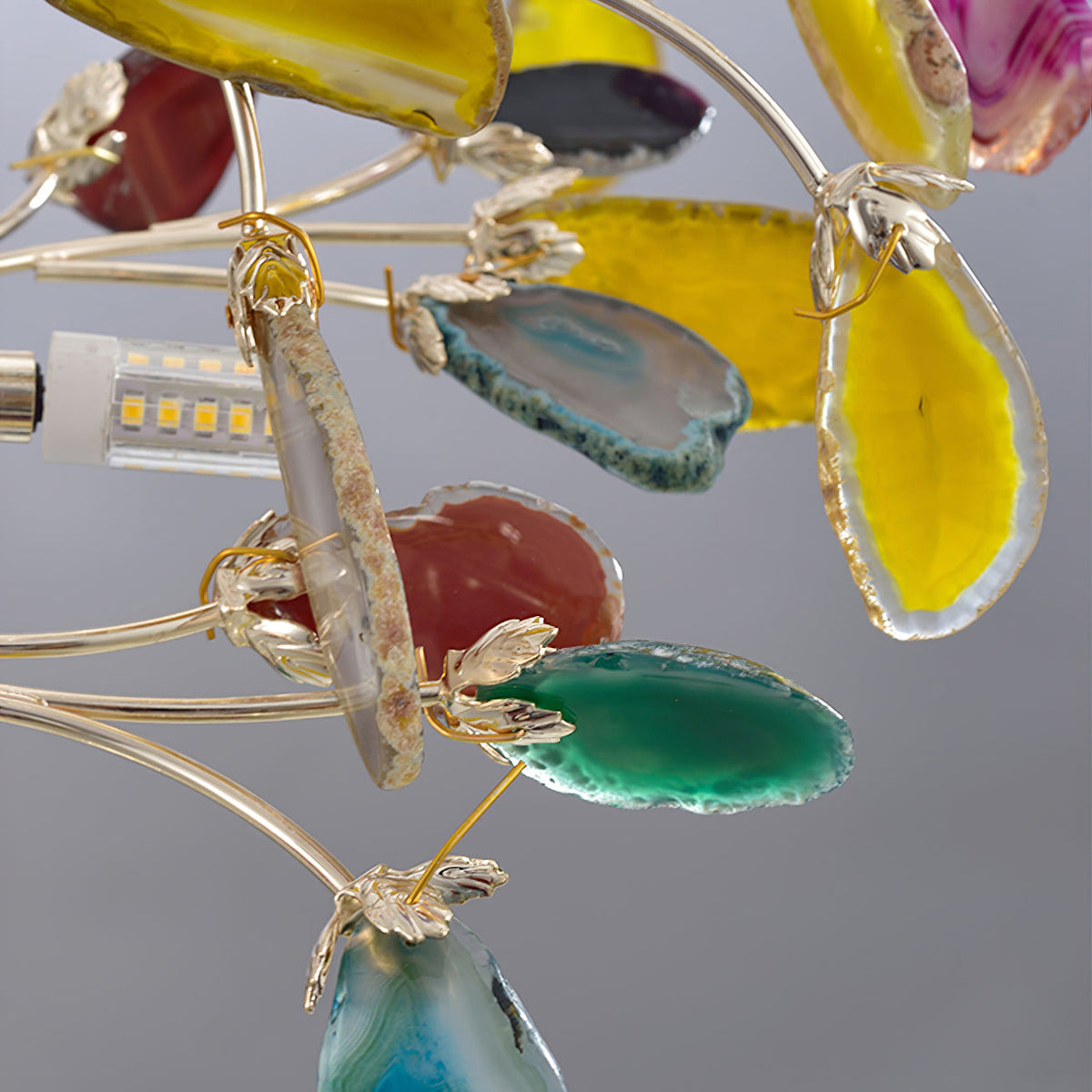 Close view of yellow, green and blue agate slices held on gold branch clips on this Clérachic floor lamp, with a bulb at left.