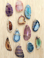 Wire-wrapped agate slice pendants in several colours laid out on a pale wood board, shown as a reference for this Clérachic floor lamp's stone.