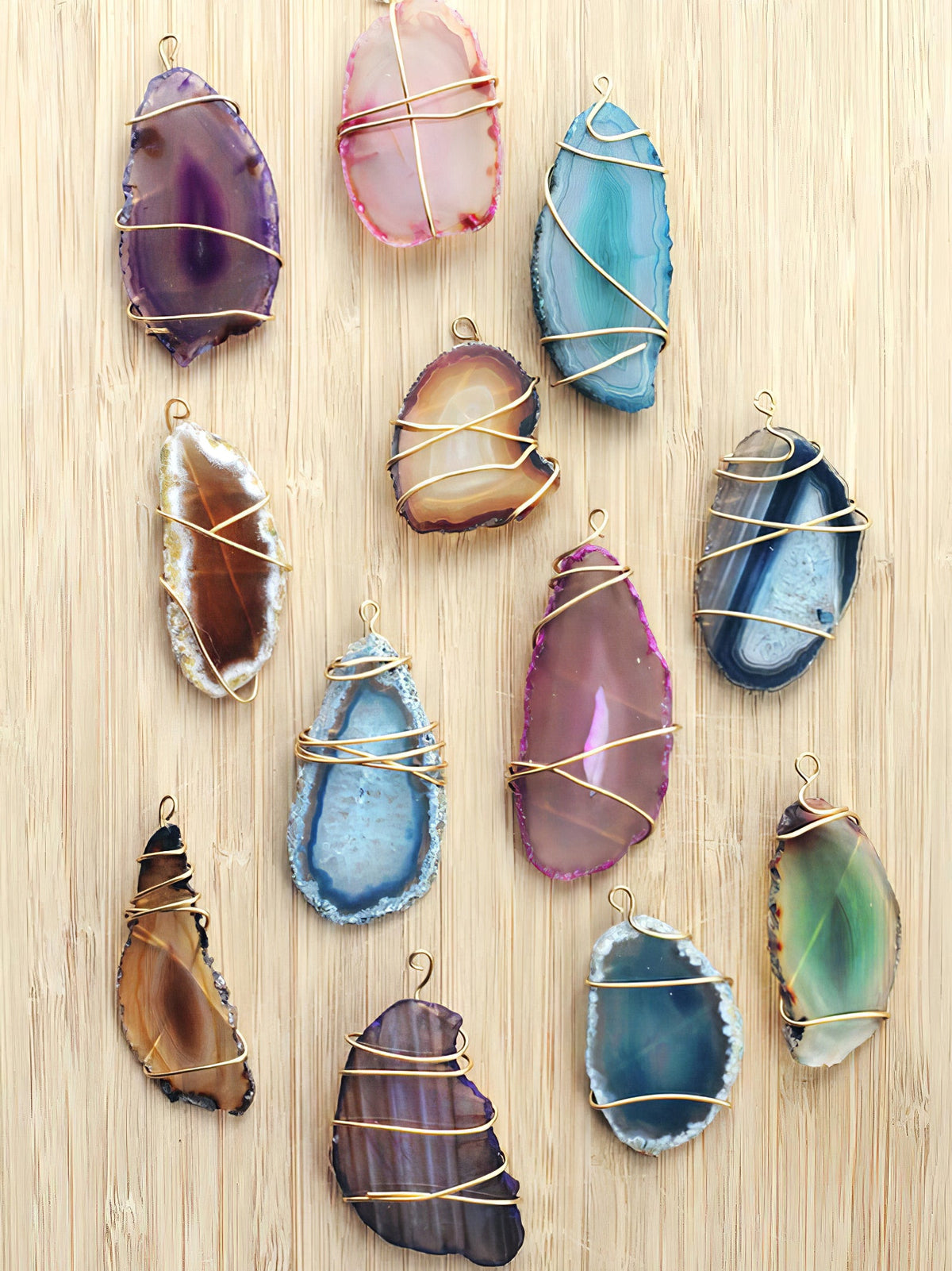 Wire-wrapped agate slice pendants in several colours laid out on a pale wood board, shown as a reference for this Clérachic floor lamp's stone.