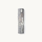 Tall half-cylinder wall light in rough grey stone-look resin, with a jagged crack glowing white, on a plain white backdrop, from Clérachic.