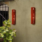 Two red stone-look wall lights glow through their cracks on a sage-coloured garden wall beside green hydrangea leaves, from Clérachic.