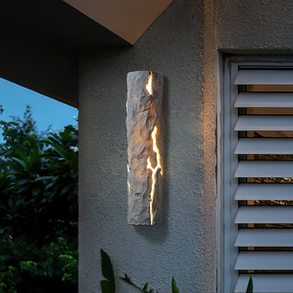Grey textured wall light under an overhang beside louvred shutters, light spilling from its cracks, a Clérachic outdoor wall light.