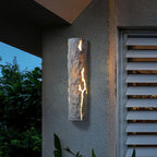 Grey textured wall light under an overhang beside louvred shutters, light spilling from its cracks, a Clérachic outdoor wall light.