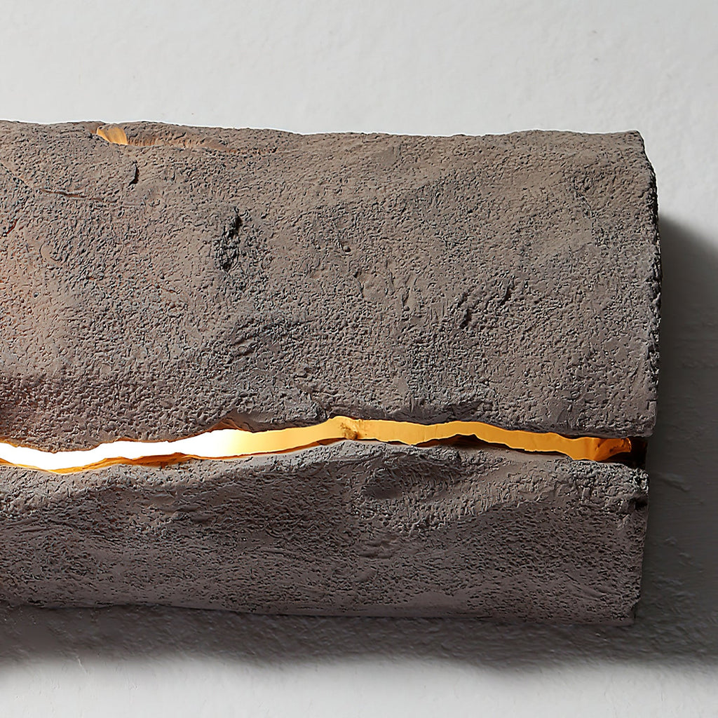 Close view of the rough grey-brown surface and a glowing horizontal crack on this Clérachic wall light.