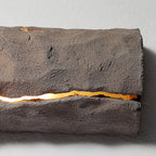 Close view of the rough grey-brown surface and a glowing horizontal crack on this Clérachic wall light.