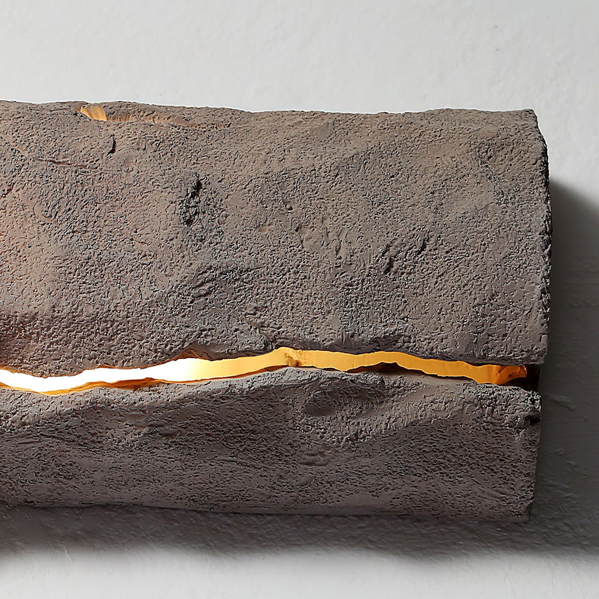 Close view of the rough grey-brown surface and a glowing horizontal crack on this Clérachic wall light.