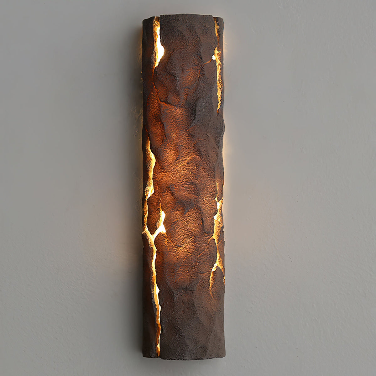 Dark brown textured wall light glowing amber through vertical cracks, mounted on a pale grey wall, from Clérachic.