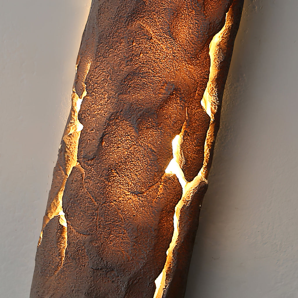 Angled close view of the pitted stone-look surface lit amber along its cracks, on this Clérachic wall light.