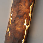Angled close view of the pitted stone-look surface lit amber along its cracks, on this Clérachic wall light.