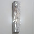 Pale grey stone-look wall light with cool white light pouring through its cracks, on a light wall, from Clérachic.