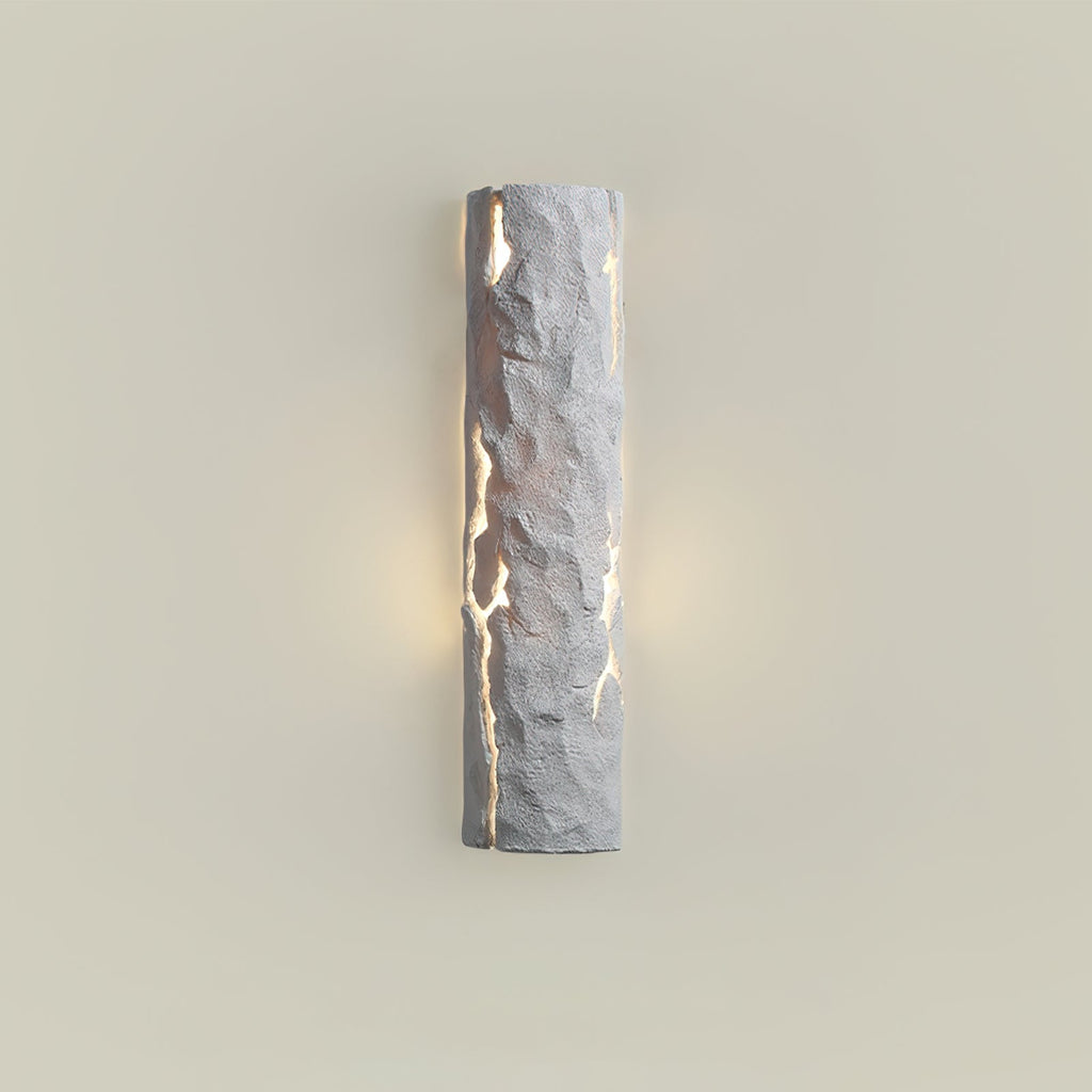 Grey stone-look wall light with soft warm light at its sides on a cream wall, a Clérachic wall light.