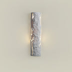 Grey stone-look wall light with soft warm light at its sides on a cream wall, a Clérachic wall light.