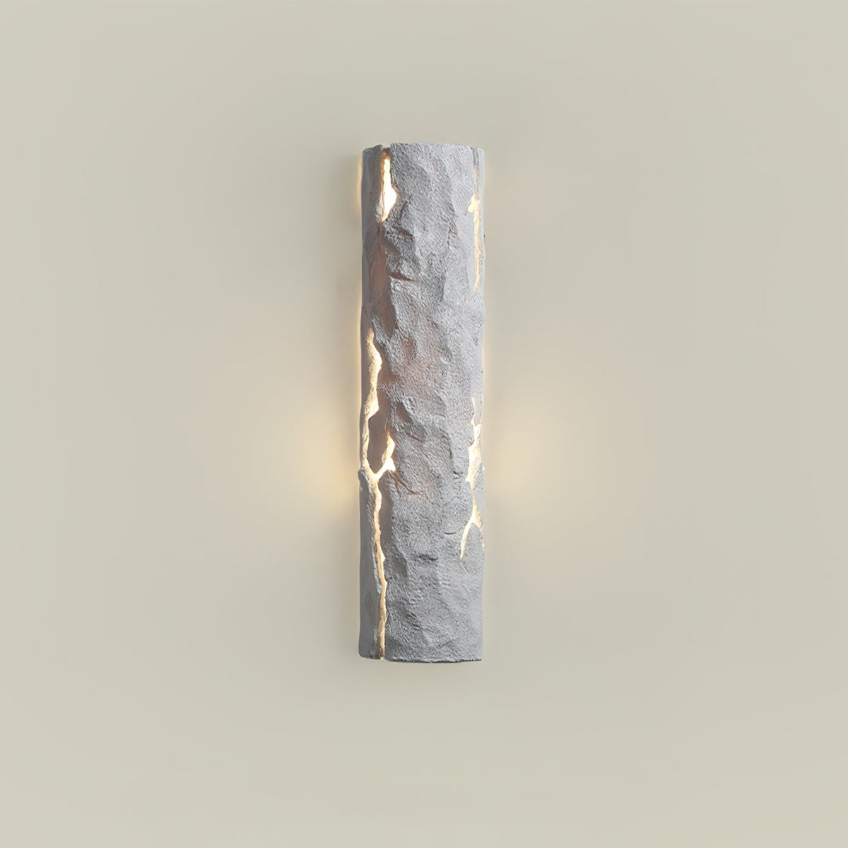 Grey stone-look wall light with soft warm light at its sides on a cream wall, a Clérachic wall light.