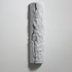 Unlit pale grey wall light with a deep dark crack down its centre, on a light grey wall, from Clérachic.