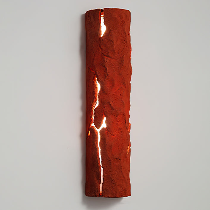 Red stone-look wall light with cracks glowing white, mounted on a pale grey wall, a Clérachic wall light.