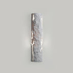 Pale grey stone-look wall light with soft light leaking from the cracks on a grey wall, from Clérachic.