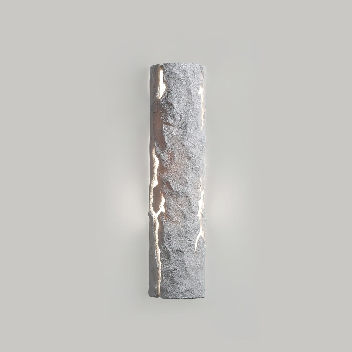 Pale grey stone-look wall light with soft light leaking from the cracks on a grey wall, from Clérachic.