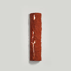 Red stone-look wall light with a glowing white crack, on a pale grey wall with a faint shadow, a Clérachic wall light.