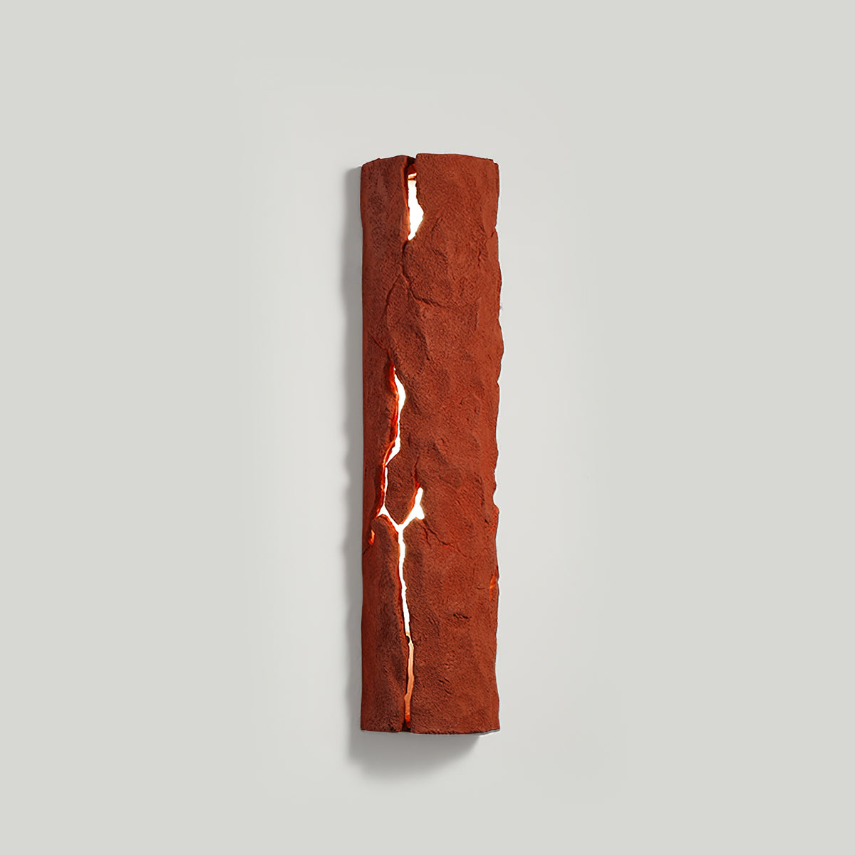 Red stone-look wall light with a glowing white crack, on a pale grey wall with a faint shadow, a Clérachic wall light.
