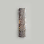 Taupe-grey stone-look wall light lit softly through cracks on a pale grey wall, from Clérachic.