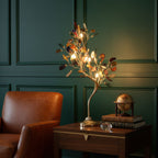 Lit, this Clérachic agate-leaf table lamp stands on a dark wooden side table beside a leather armchair and a green panelled wall.