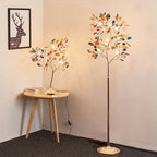 Corner of a room with the Clérachic table lamp on a round wooden side table and a taller floor version of the same tree beside it.