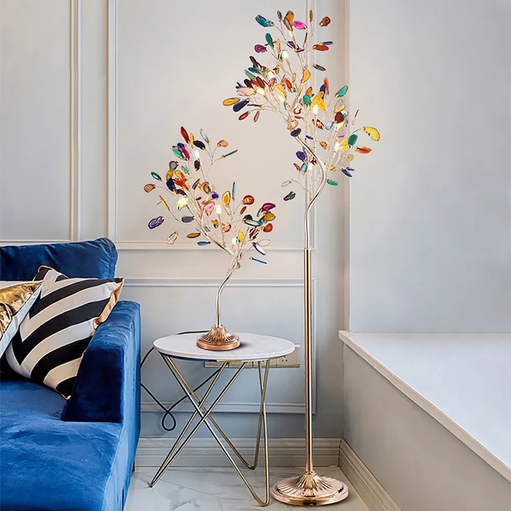 The Clérachic agate tree lamp shown as both a table lamp on a glass side table and a tall floor lamp, next to a blue sofa.