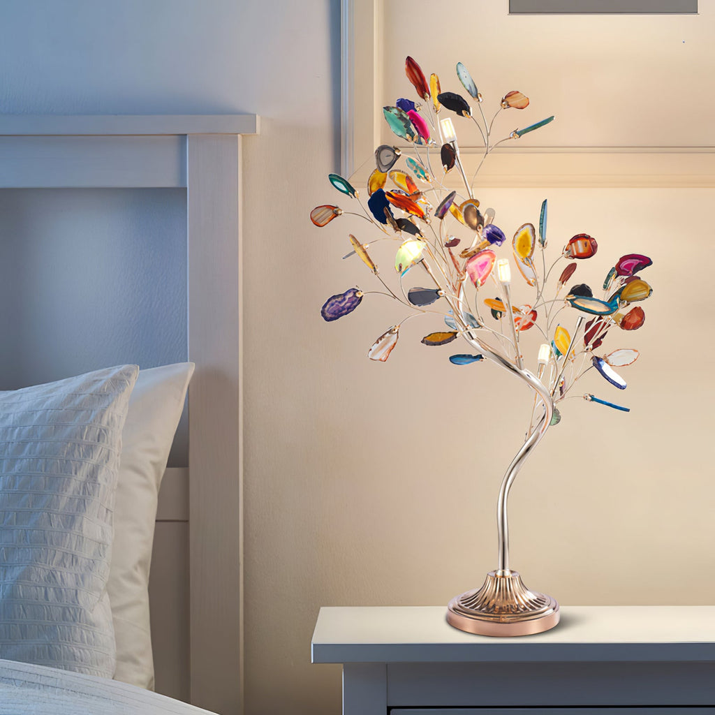 This Clérachic agate-leaf table lamp is lit on a pale bedside table, with white pillows and a light headboard behind it.