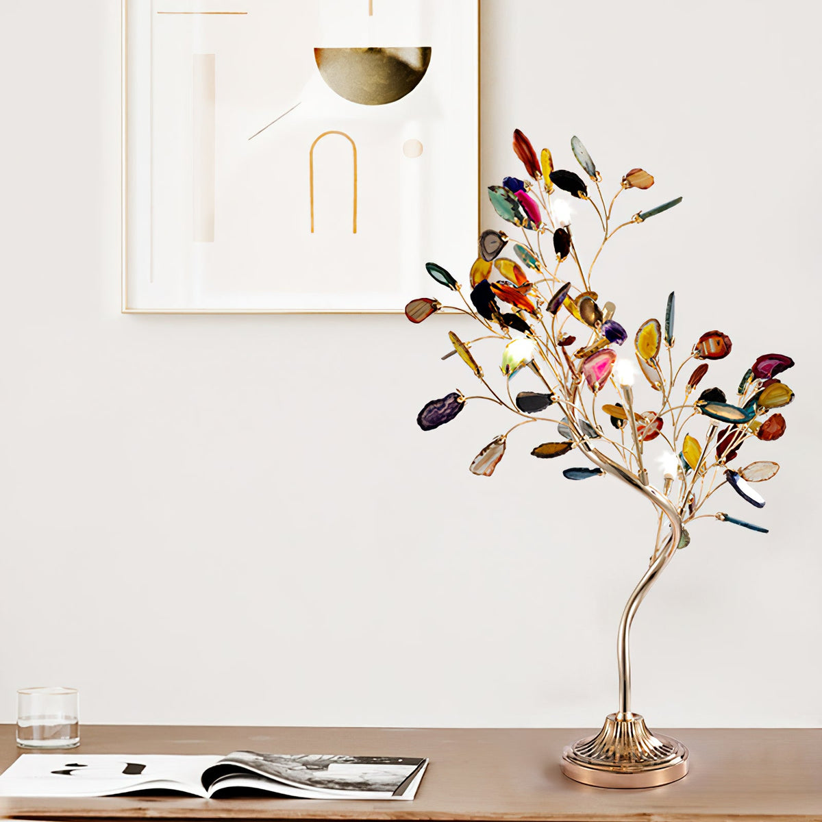Slim curving stem and a bushy crown of coloured agate slices on this Clérachic table lamp, on a wooden shelf beside a magazine.