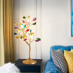 A lit Clérachic tree table lamp on a dark side table, with a blue tufted sofa and a houndstooth cushion nearby.