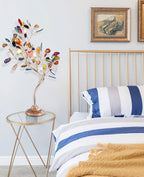 A Clérachic agate tree lamp on a glass side table, with a brass bed frame and blue-and-white striped bedding behind.
