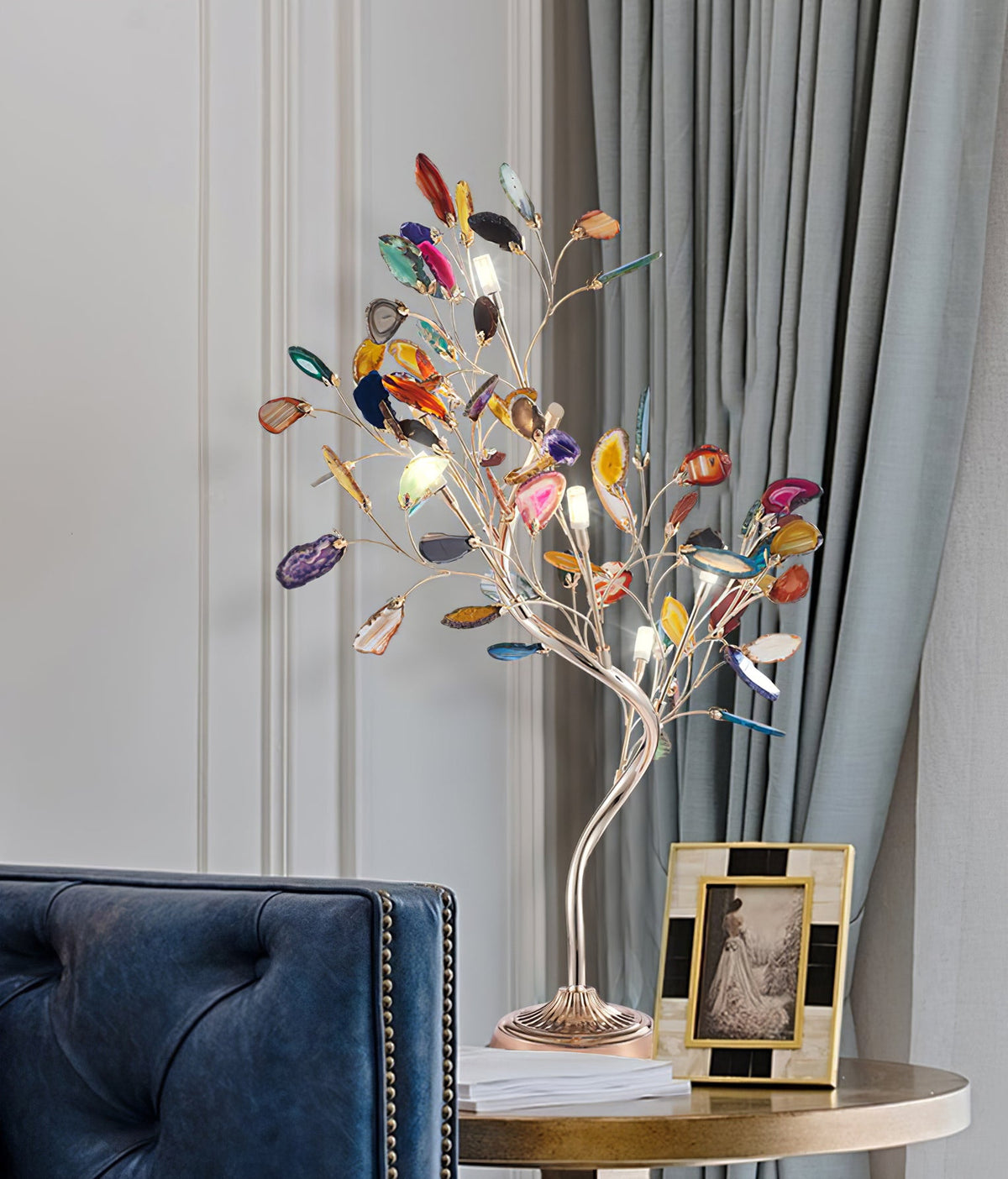 This Clérachic table lamp stands on a round brass side table in front of grey curtains, with a framed photo at its base.