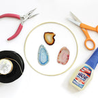 Three loose agate slices on a white table with pliers, scissors, a gold ring and a tube of glue, shown for this Clérachic lamp.