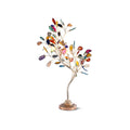 A Clérachic table lamp on white, with multicoloured agate leaves on a slim, curved gold stem above a bronze fluted base.