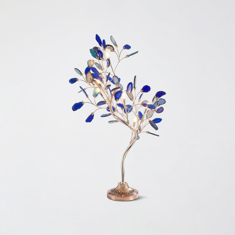 A Clérachic tree table lamp with blue agate leaves lit among its branches, on a pale grey backdrop.