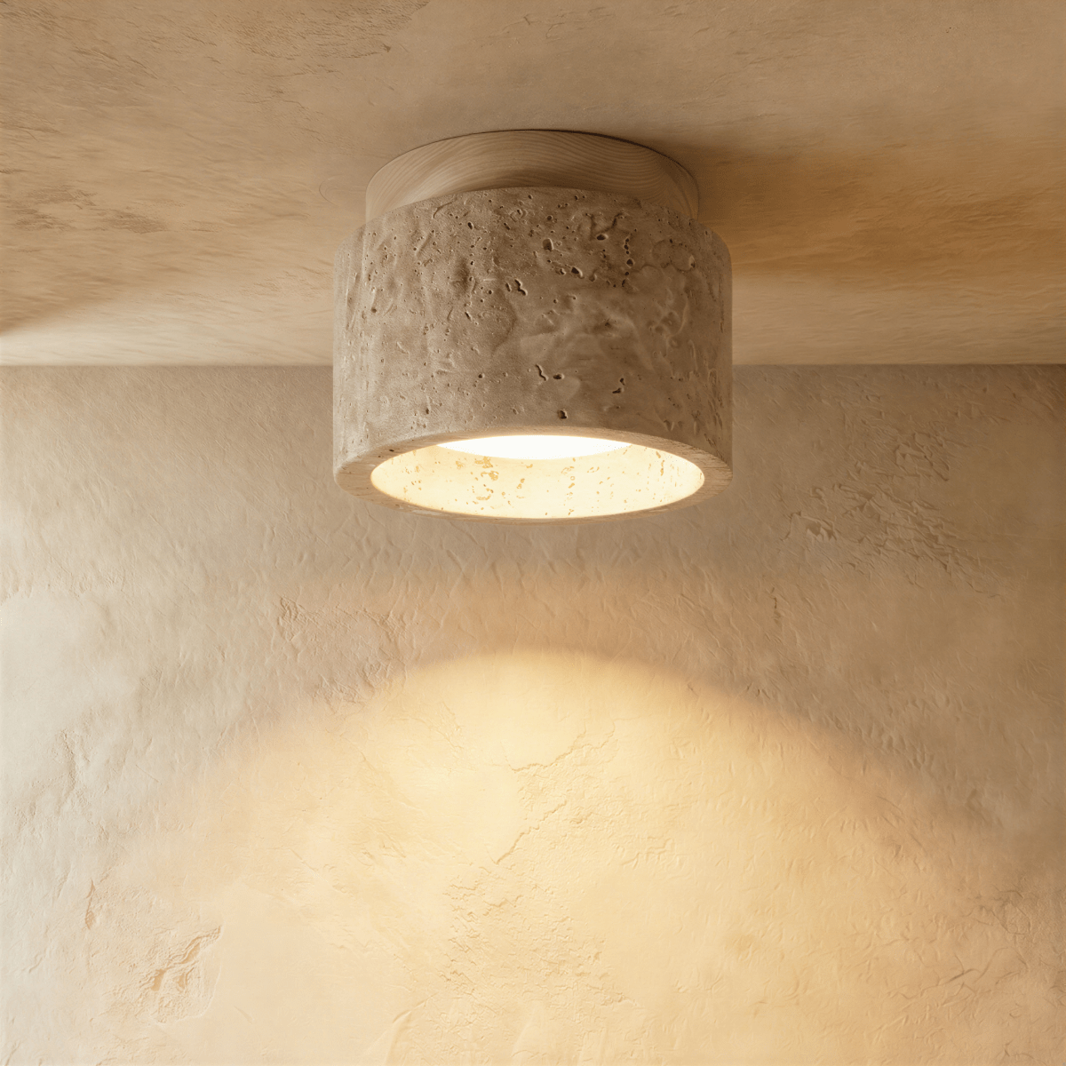 Clérachic compact drum ceiling light in pitted travertine with a pale wood canopy, casting a soft pool of warm light on plaster.