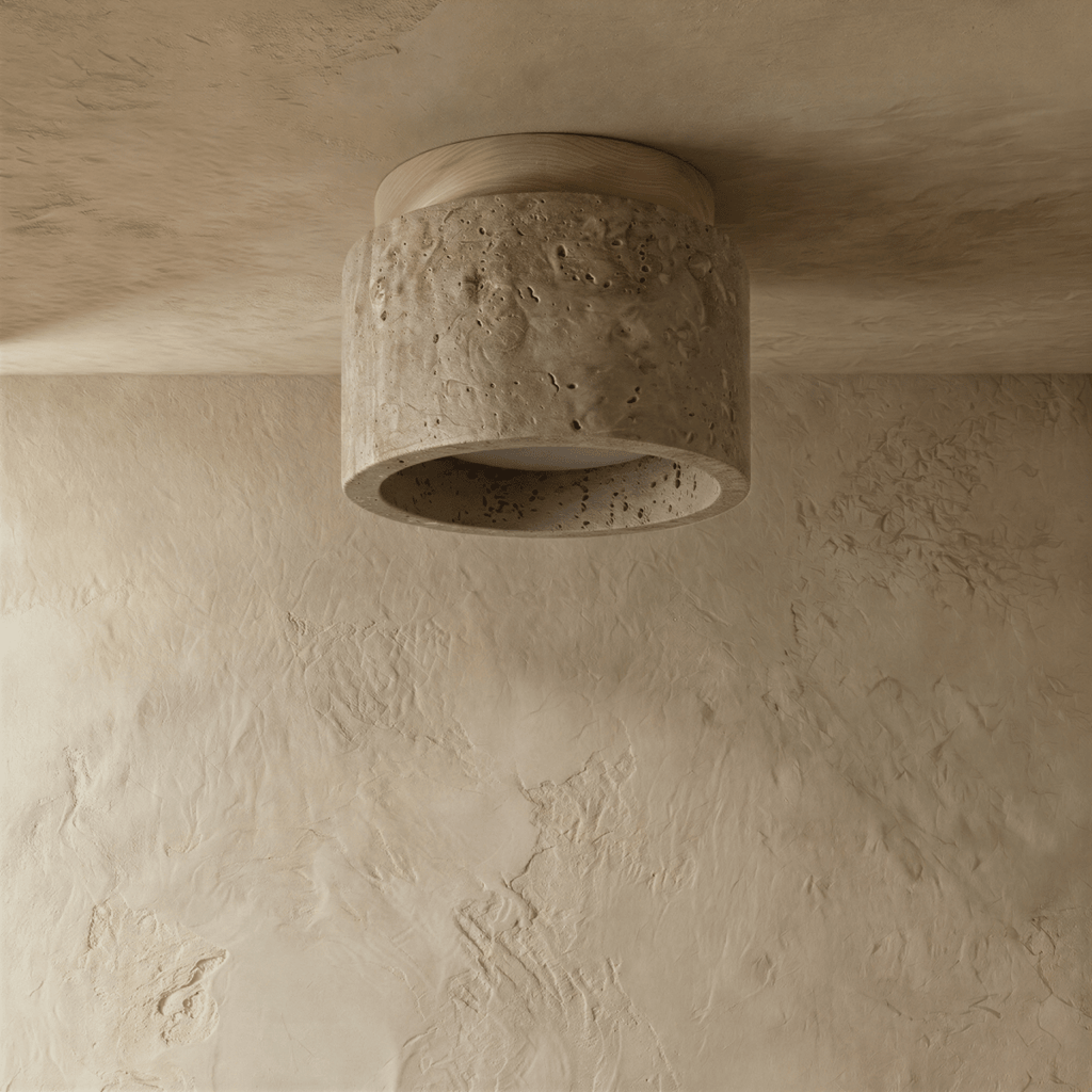Clérachic compact drum ceiling light switched off, pitted travertine body with a pale wood canopy on a plaster ceiling.