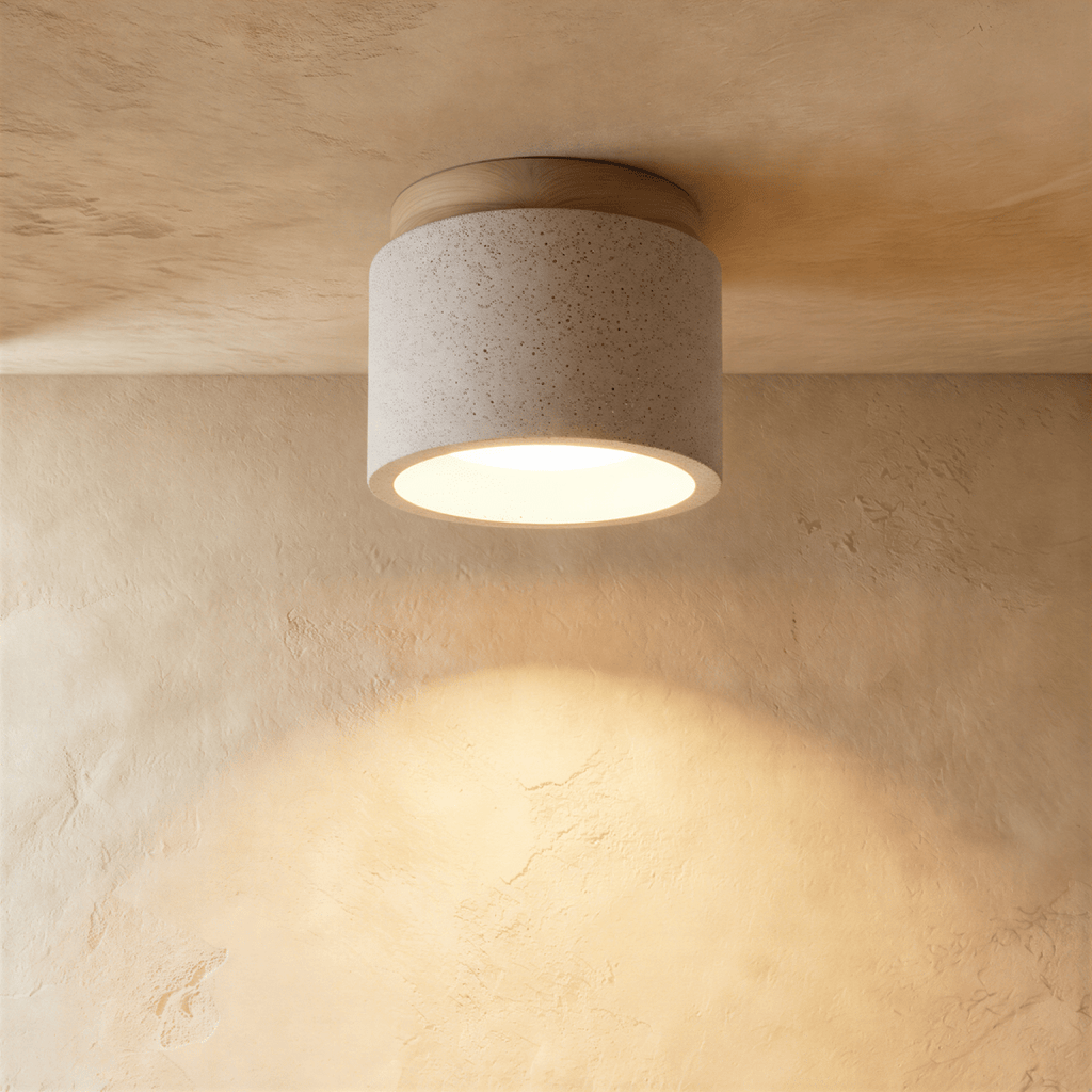 Clérachic compact drum ceiling light in speckled white cement with a pale wood canopy, lit warm over a limewashed wall.