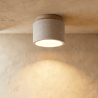 Clérachic compact drum ceiling light in speckled white cement with a pale wood canopy, lit warm over a limewashed wall.