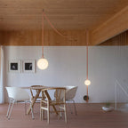 Two single globes from the Clérachic Strap-Hung Glass Globe Pendant Light hung individually over a wooden dining area, lit at different heights.