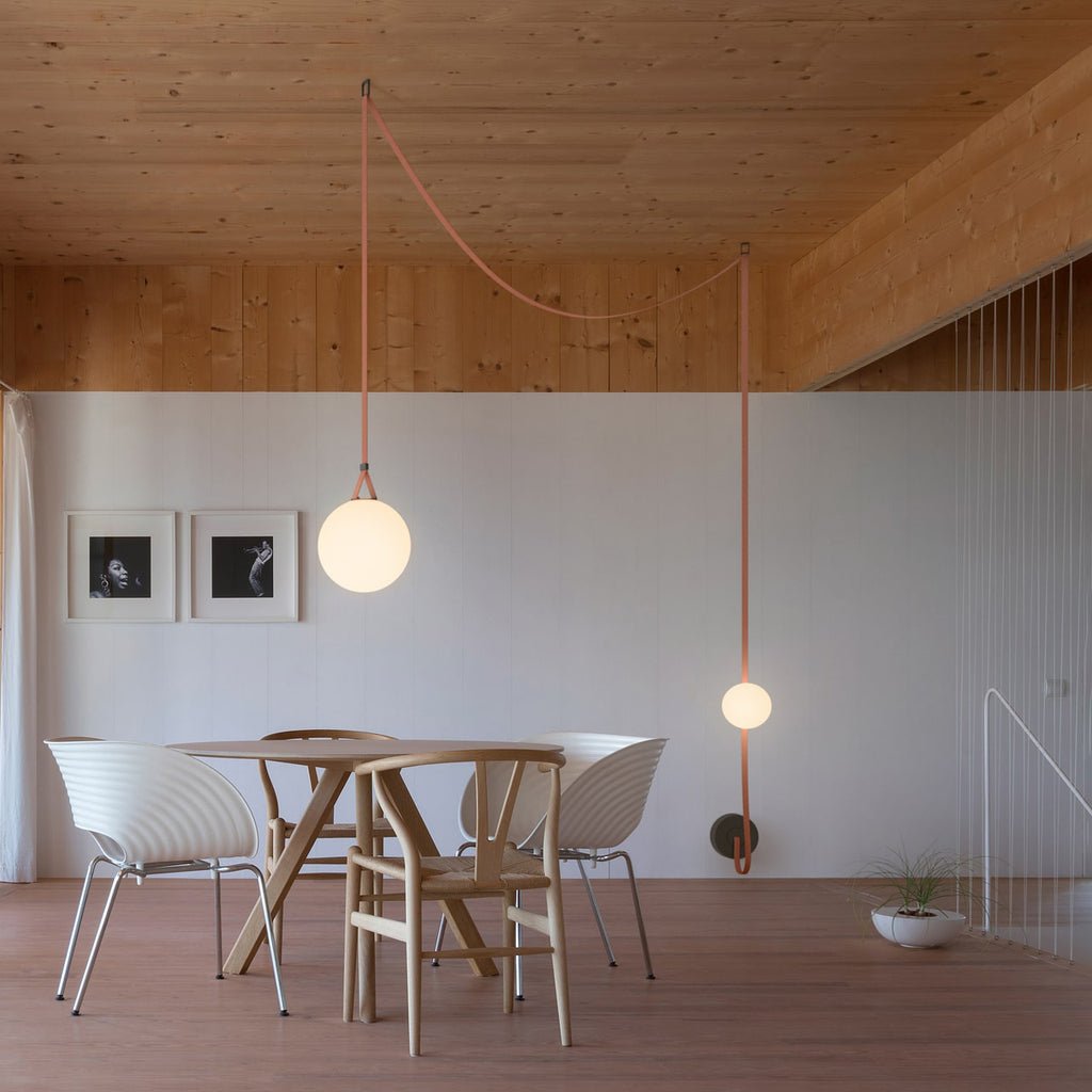 Two single globes from the Clérachic Strap-Hung Glass Globe Pendant Light hung individually over a wooden dining area, lit at different heights.