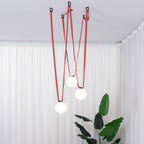 Another angle of the Clérachic Strap-Hung Glass Globe Pendant Light's red canvas globes hanging in front of sheer curtains, with an ottoman edge visible below.