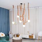 Wide living-room view of the Clérachic Strap-Hung Glass Globe Pendant Light in orange leather, its globes glowing between a blue curtain and a green sofa.